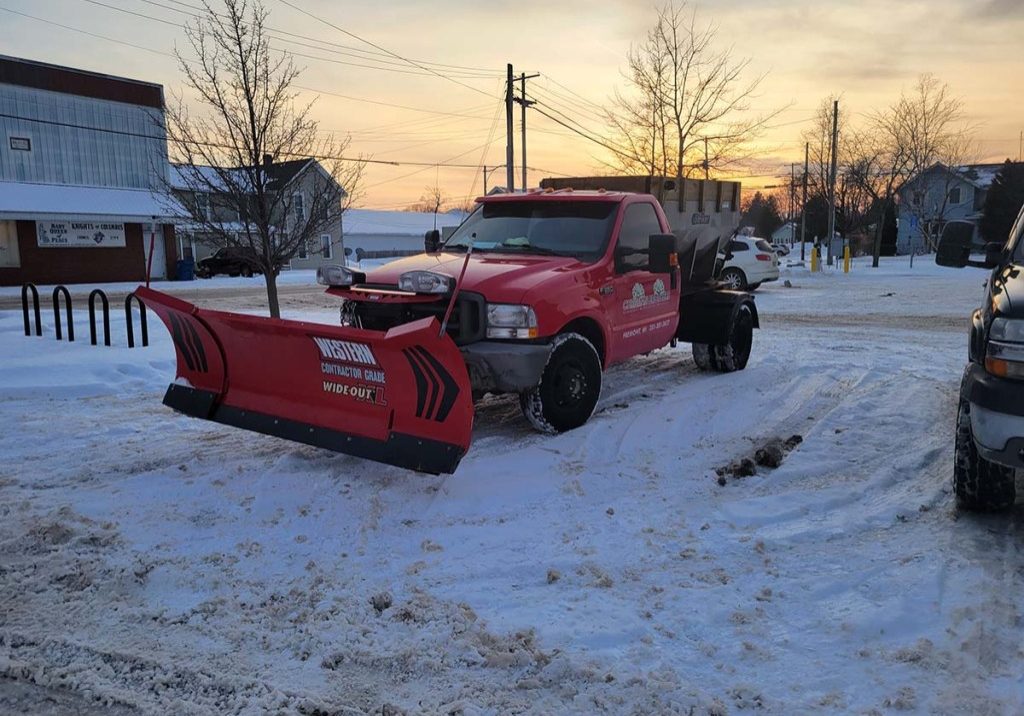 Christian Brothers plow truck in a plowed parking lot before dawn on a snowy day