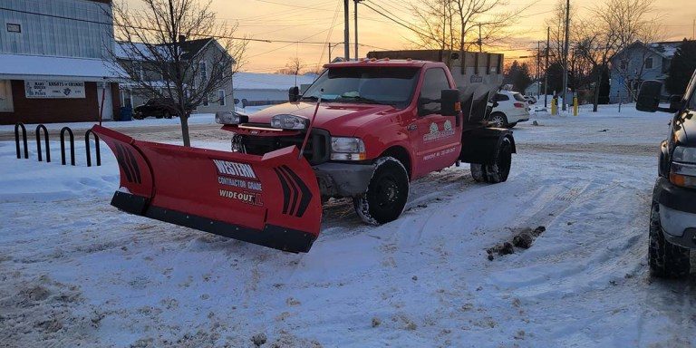 Christian Brothers plow truck in a plowed parking lot before dawn on a snowy day